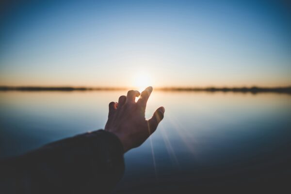 a hand reaching out into the sunset as a symbolism of hope