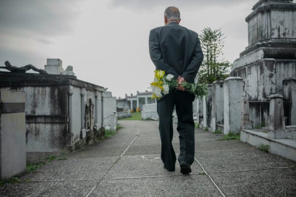 a man walking with a bouquet of flowers through a cemetery