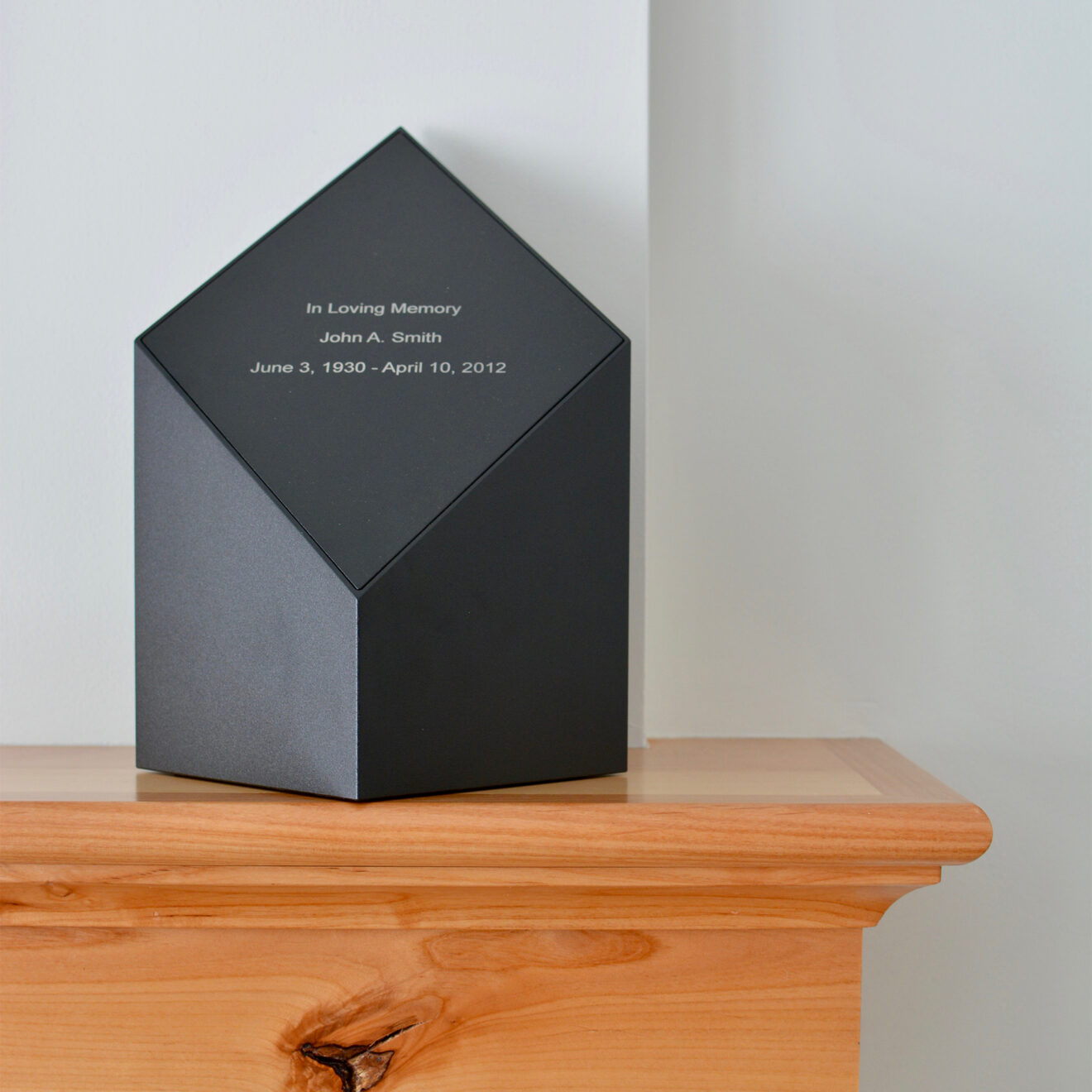 A laser engraved black everlast series modern cremation urn with a black face sitting on a mantel.