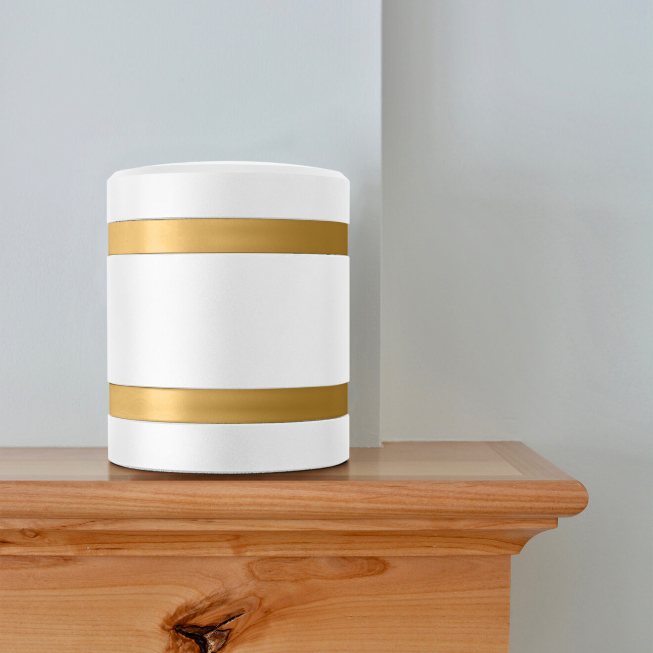 a white metal infinite series modern cremation urn with gold bands sitting on a mantel.
