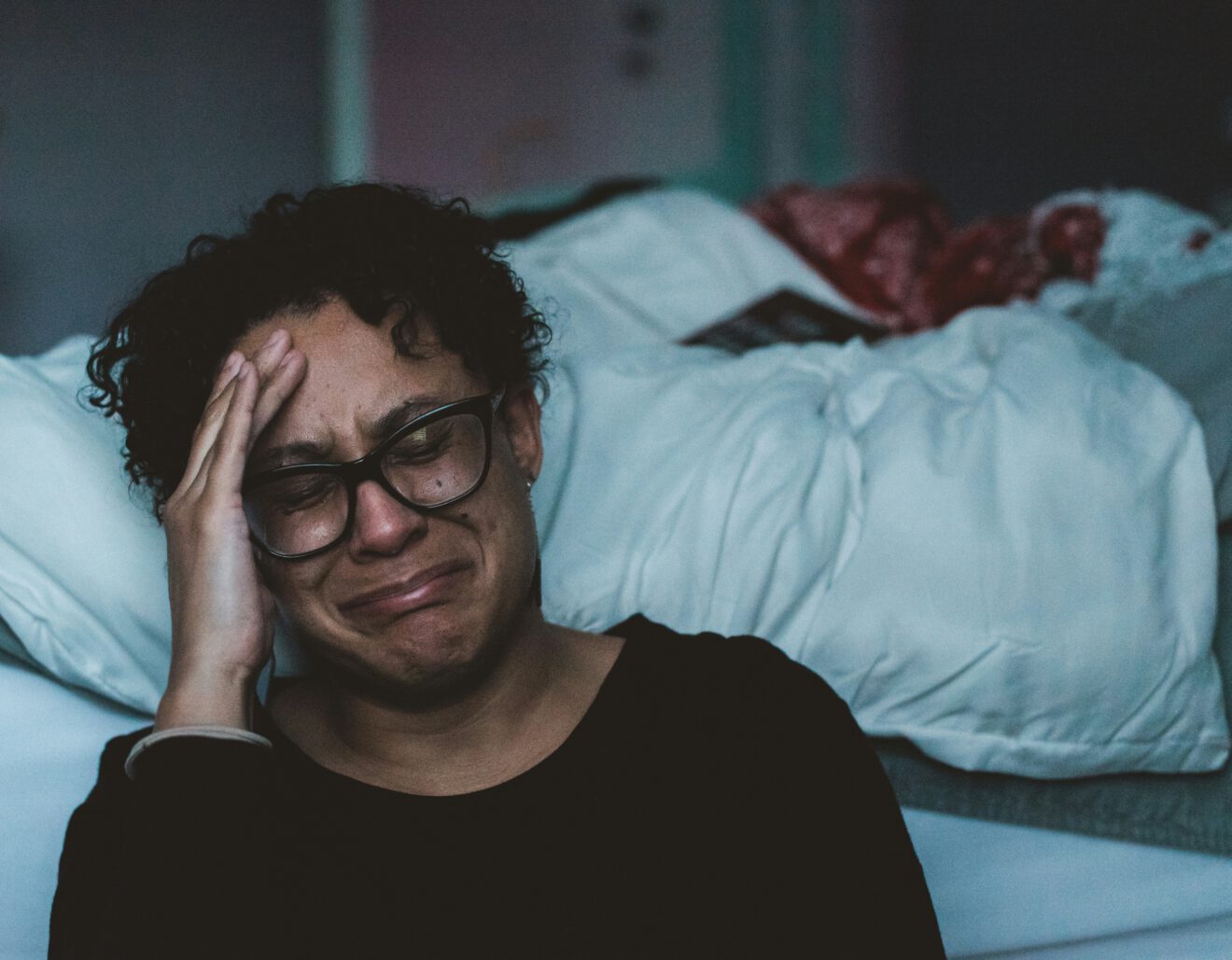 a woman on the floor by her bed, expressing emotions through tears