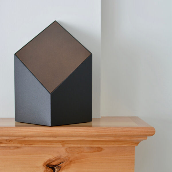 A black everlast series modern cremation urn with a bronze face sitting on a mantel.