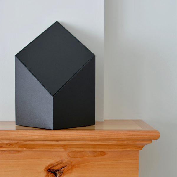 A black everlast series modern cremation urn with a black face sitting on a mantel.